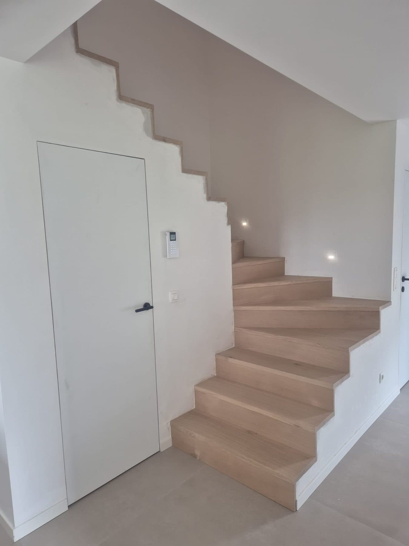 Escalier en chêne et porte invisible dans un hall blanc